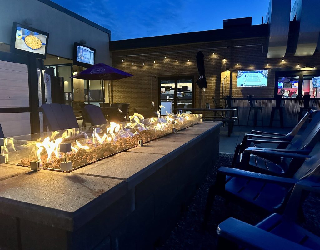The Rock Garden patio at dusk with a long fire pit, seating, and outdoor TVs.